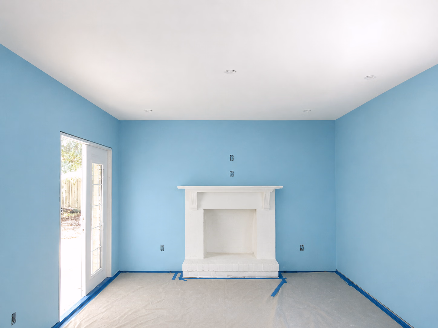 Empty room with newly painted light blue walls, white fireplace, and floor covered with protective plastic.