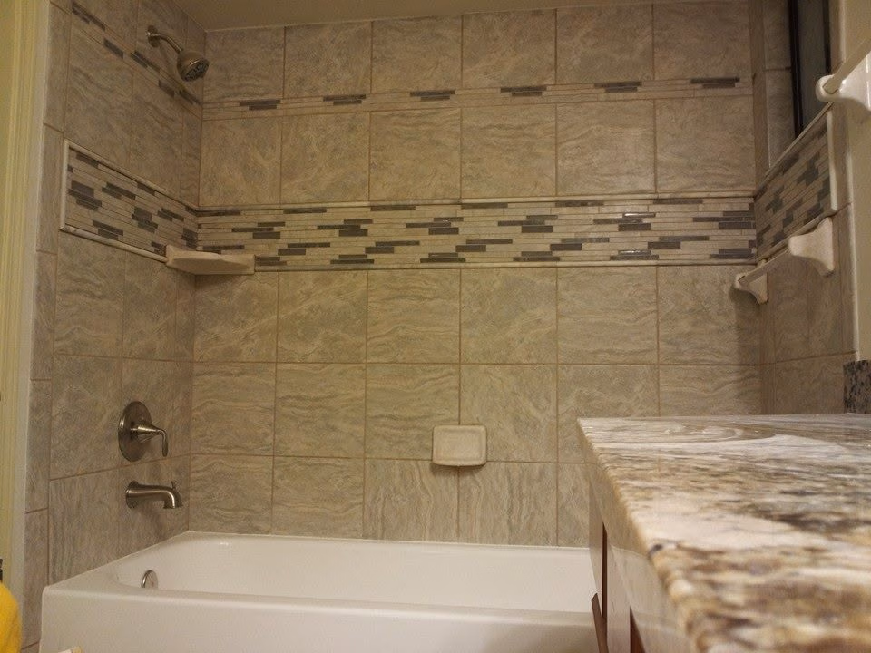 Bathroom with beige tiled shower and bathtub, granite countertop, chrome faucet, and soap holders.