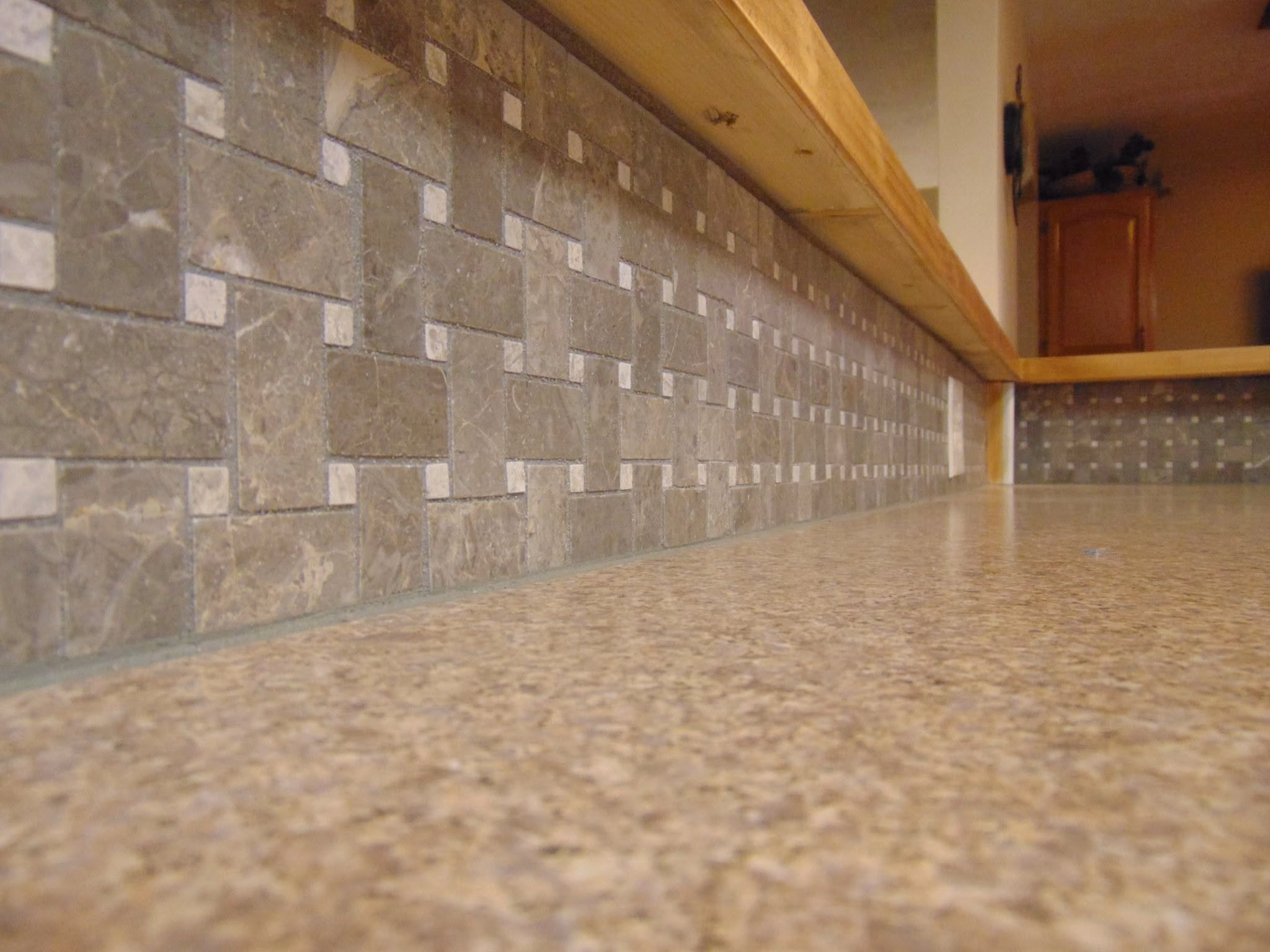Close-up of a kitchen countertop with a brown patterned tile backsplash and wood trim above.