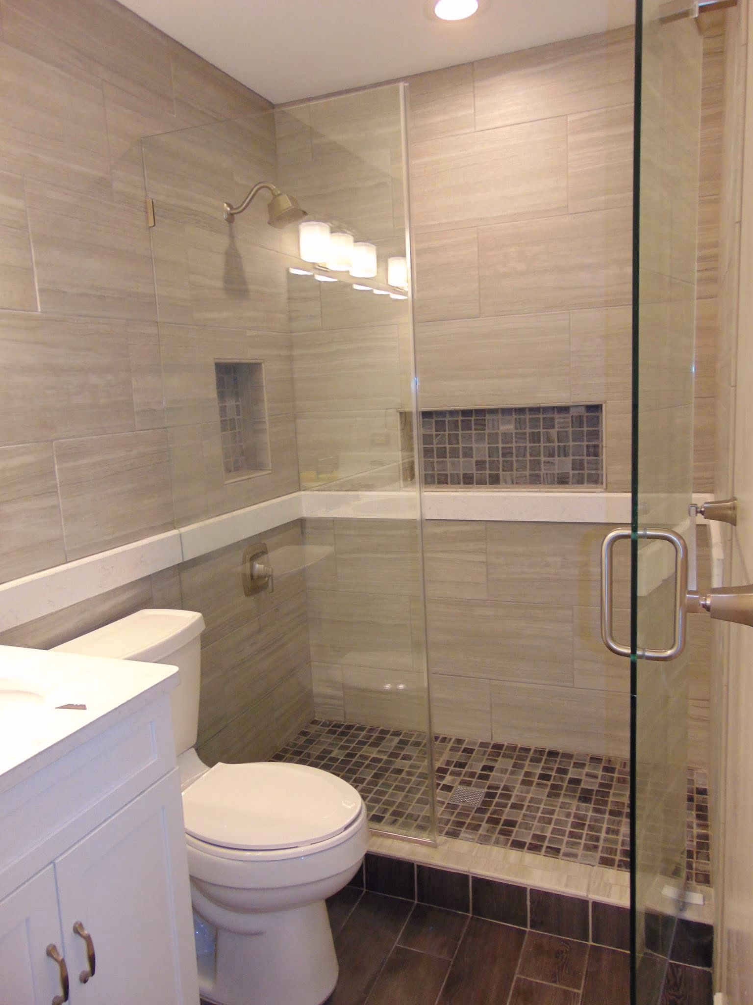 Modern bathroom with glass shower enclosure, tiled walls and floor, white toilet, and vanity cabinet.