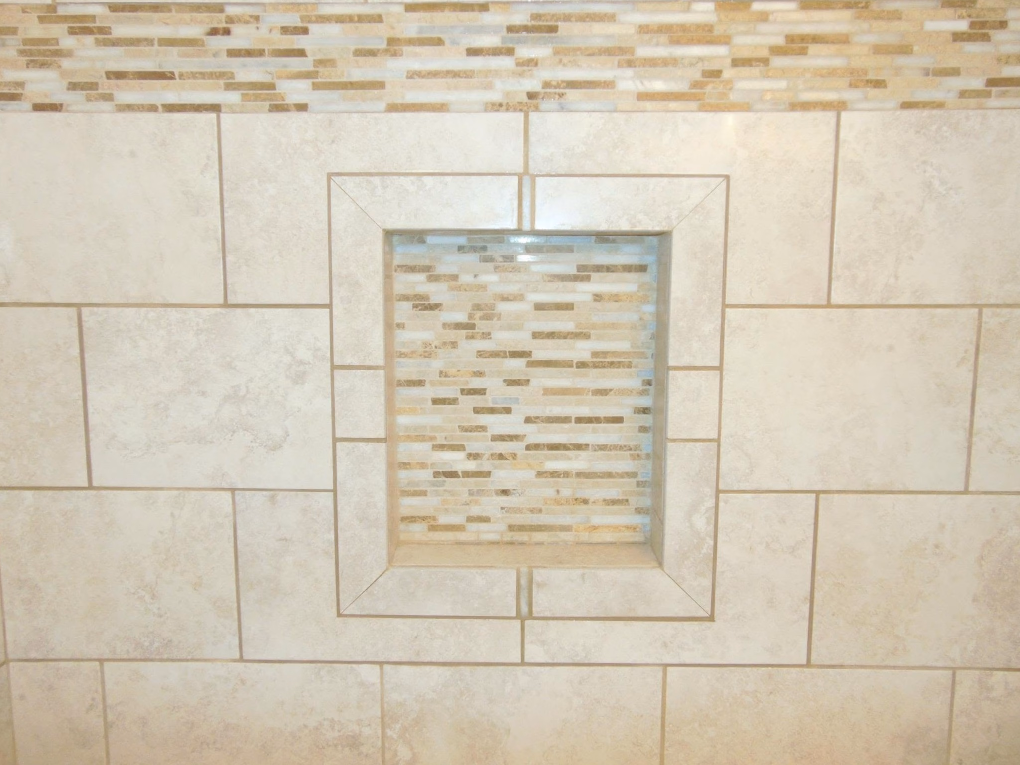 Wall with beige ceramic tiles and a square inset of smaller mosaic tiles in the center.