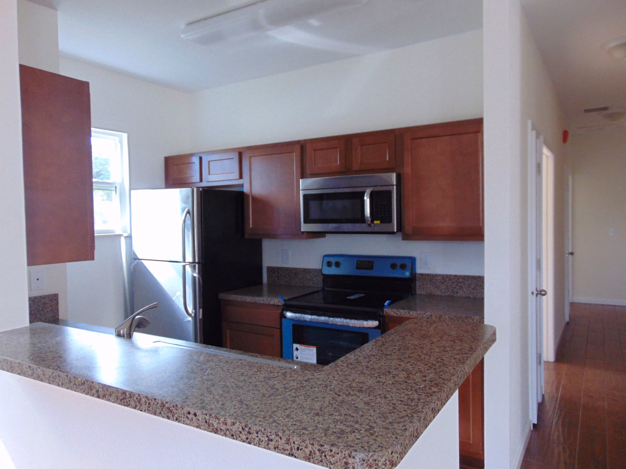 Kitchen with brown cabinets, granite countertops, stainless steel refrigerator, stove, and built-in microwave.