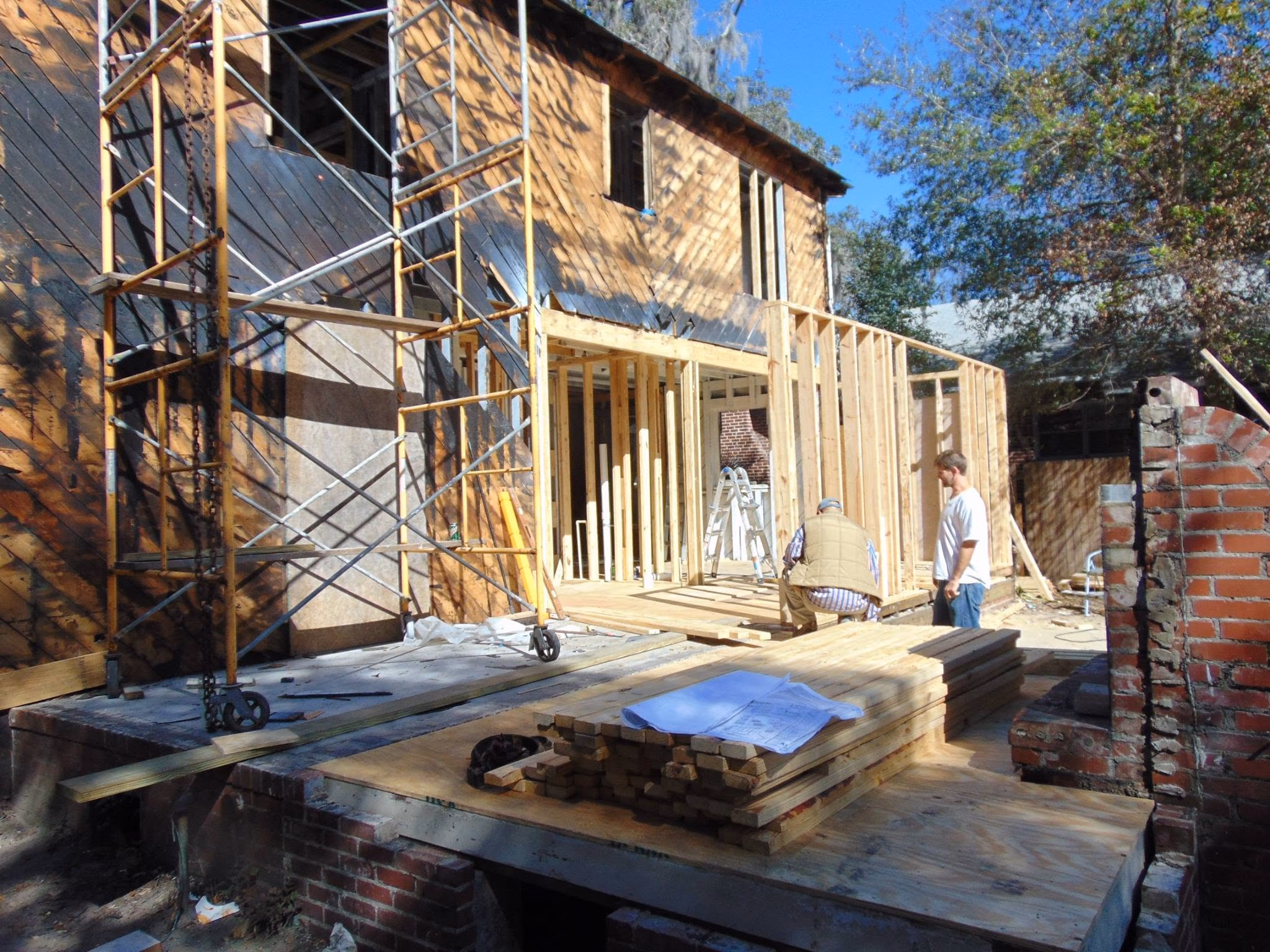 Two men working on wooden framing of a house under construction on a sunny day.