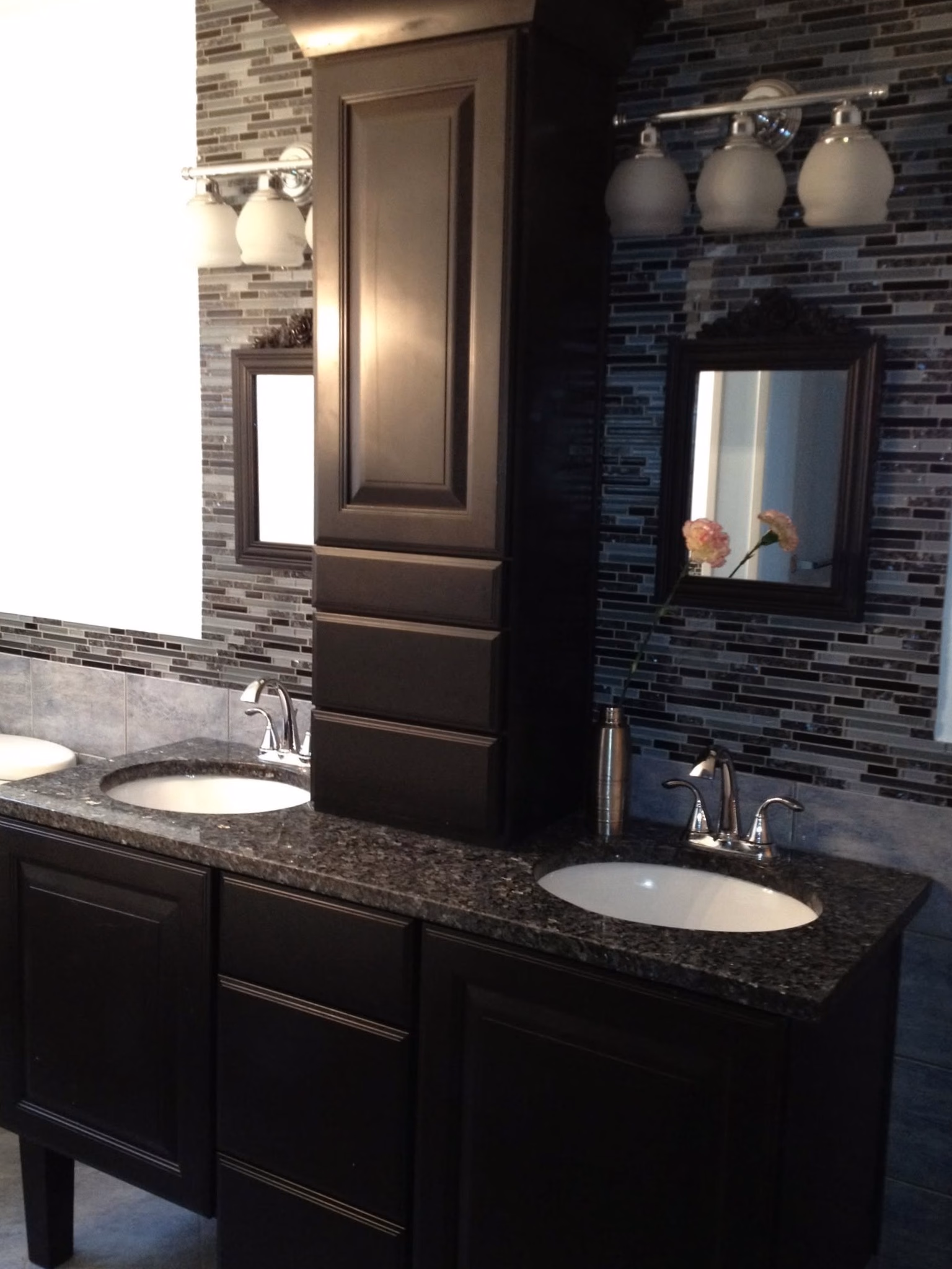Modern double bathroom vanity with dark cabinets, granite countertop, two sinks, mirrors, and light fixtures.