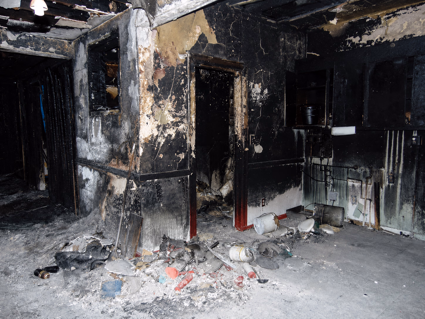 Room severely damaged by fire with charred walls and debris scattered on the floor.