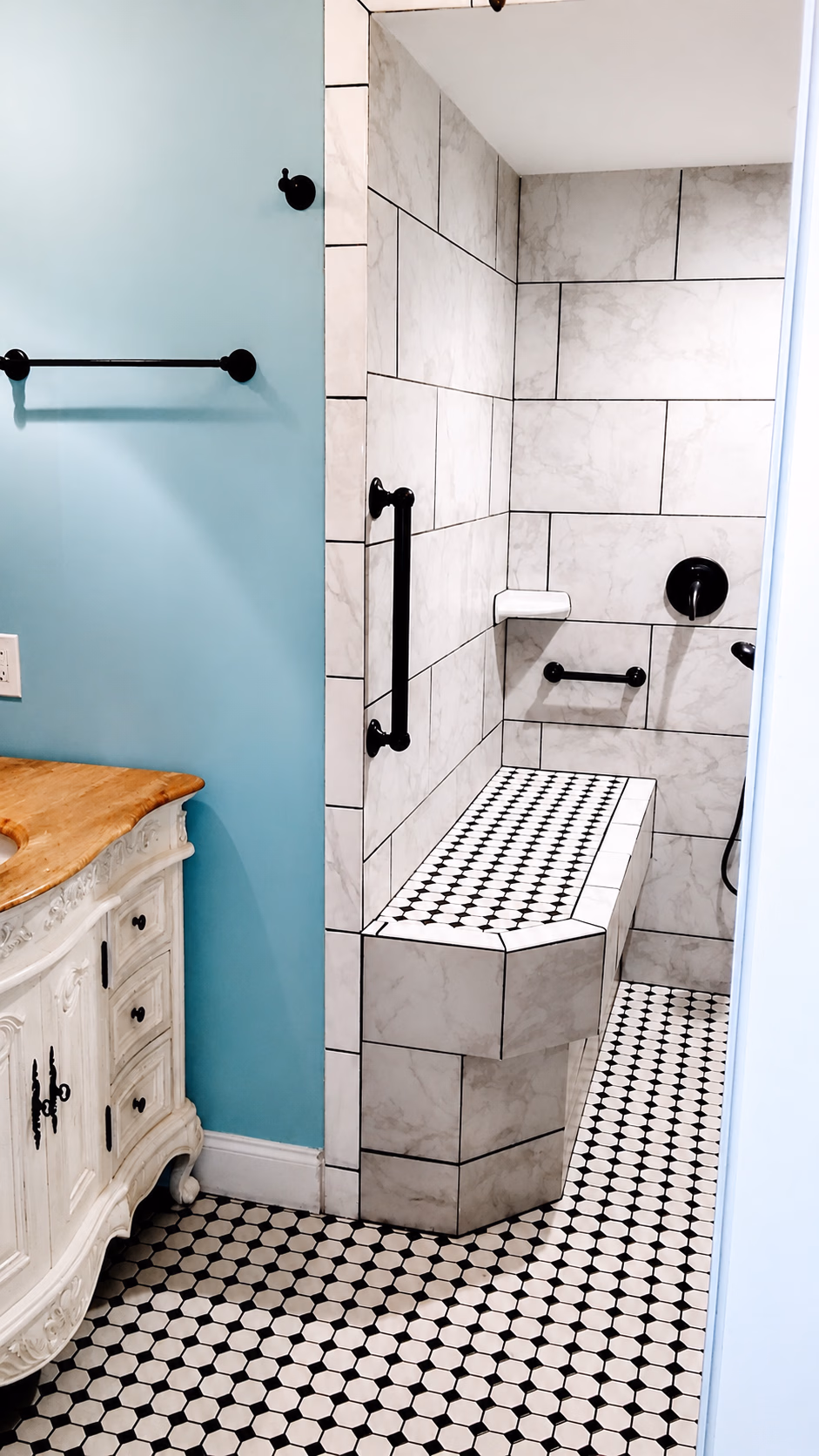Bathroom with marble tile walk-in shower, built-in bench, black grab bars, and vintage wood vanity.